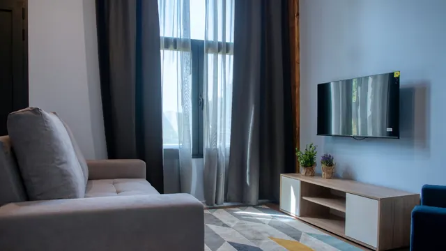 Sala com sofá, televisão e janelas altas com cortinados