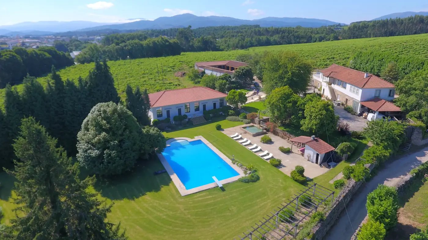 Vista aérea da piscina rodeada de relva, com espreguiçadeiras e as casas de telhado vermelho