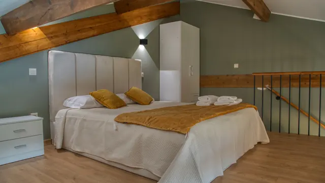 Quarto de casal em tons de oliveira, com almofadas mostarda e vigas de madeira